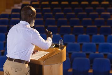 A man at a lecturn with a mic in front of an empty auditorium