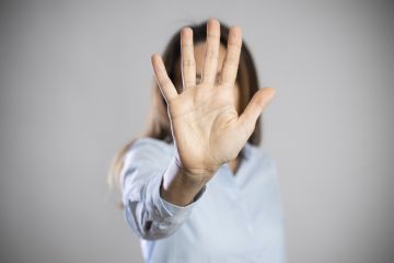 A woman holds her hand out in front of her face to say 'stop' A woman holds her hand out in front of her face to say 'stop'