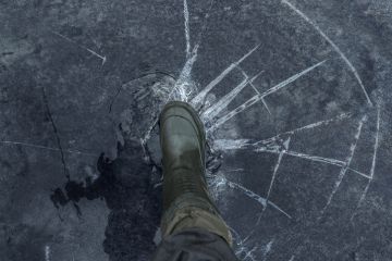 Fisherman foot on broken cracked thin ice at lake