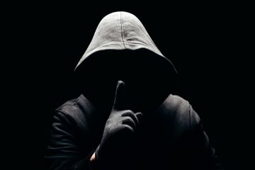 Shadowy figure with a hood holds a finger up to their face Shadowy figure with a hood holds a finger up to their face