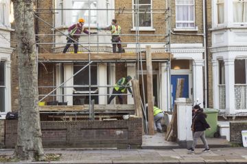 Four workers collaborate to build a scaffold during the refurbishment of a residential premises in London. Four workers collaborate to build a scaffold during the refurbishment of a residential premises in London.