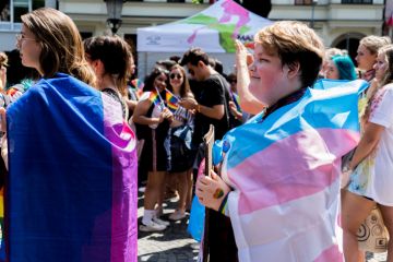 A woman at a demonstration is draped in an LGBTQ flag