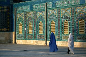 The Blue Mosque in Mazar-i-Sharif, Balkh Province in Afghanistan The Blue Mosque in Mazar-i-Sharif, Balkh Province in Afghanistan. Two women wearing burqas (burkas) walk past a wall of the mosque adorned with colorful tiles and mosaics. Northern Afghanistan.