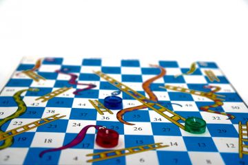 Snakes and ladders board with one counter at the top of a snake, another at the foot of a ladder