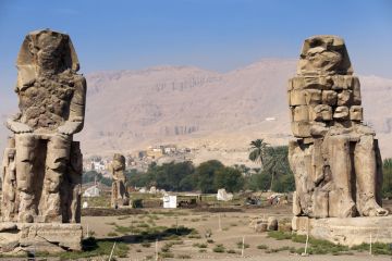 Colossi of Memnon, Luxor, River Nile, Egypt. Two massive stone statues of the Pharaoh stand at the front of the ruined Mortuary Temple of Amenhotep III