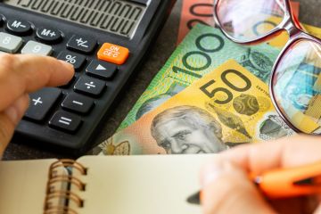 Australian dollars together with a calculator, hand writing down the results in a notebook Australian dollars together with a calculator, hand writing down the results in a notebook