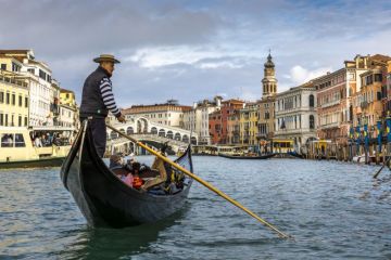 View of the beautiful Rialto Bridge spanning the Grand Canal with gondolier in foreground in Venice, Italy