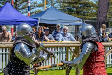 Knights in metal helmets and armor fight, a part of a costume performance at a public festival, reconstruction of knightly battles.