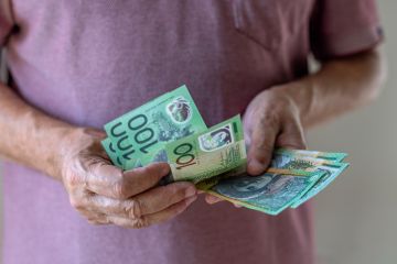 Close-up of a man counting a wad of 100 Australian dollar banknotes.