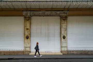 Woman walking past a closed storefront on a street in the historic center of Mexico City Woman walking past a closed storefront on a street in the historic center of Mexico City