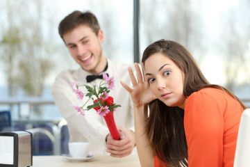 A young man offers a young woman some flowers, but she looks horrified at the camera