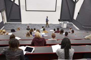 Man lectures students in lecture theatre Man lectures students in lecture theatre