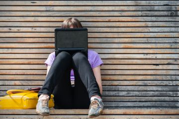 woman using a small black laptop on a bench