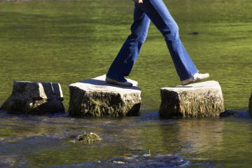 A person crossing three stepping stones on a river 
