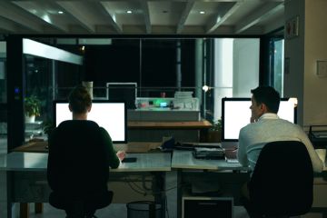 Rearview shot of two businesspeople working on computers in an office at night