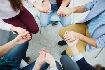 People holding hands, sitting in a circle People holding hands, sitting in a circle