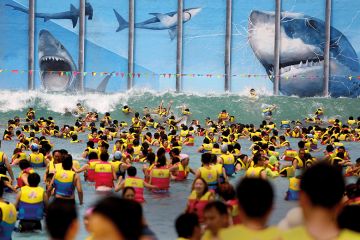 Swimmers in identical life preservers in the sea, face up to giant sharks gnashing at a metal grille