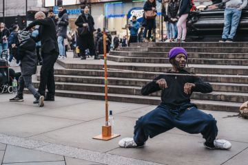 London, UK - November 24, 2019 Street performer limbo under the bar in Piccadilly Circus, one of the most popular tourist areas in London, UK, selective focus.