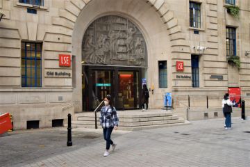 London, United Kingdom - November 13 2020 A student wearing a protective face mask walks past the LSE Old Building, London School of Economics and Political Science.