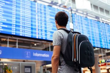 Male student looking at airport departures board Male student looking at airport departures board