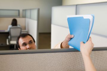 Man handing file/documents to colleague over office partition