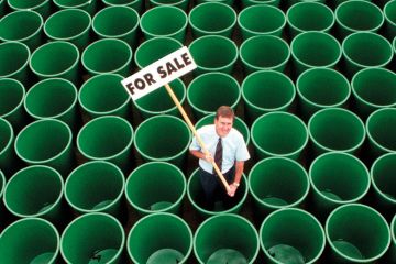 Man standing in rows of green plastic water butts, holding 'For sale' sign Man standing in rows of green plastic water butts, holding 'For sale' sign