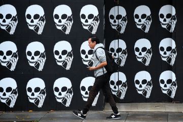 A pedestrian, using his cellphone, walks past a boarded establishment showing skeleton heads with cellphones. To illustrate that there is a delay to implementation of the lifelong learning entitlement. A pedestrian, using his cellphone, walks past a boarded establishment showing skeleton heads with cellphones. To illustrate that there is a delay to implementation of the lifelong learning entitlement.