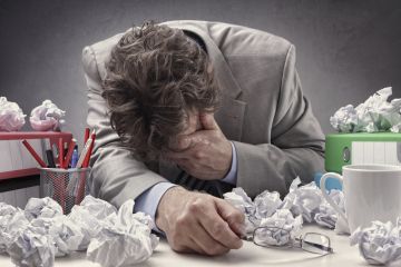 Man with head in hand surrounded by paper