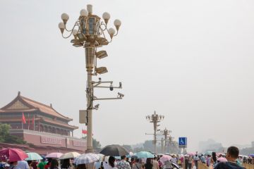 Mass tourists around the Tiananmen Gate Tower in a hot, hazy summer day in Beijing, China. Tourist attraction. Lamp post with surveillance cameras