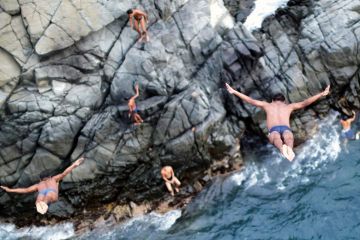 Men diving off cliff into sea