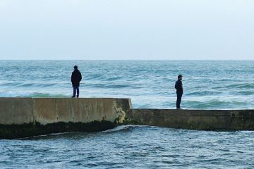 Men standing in opposite directions on seafront wall