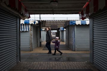 A woman and child walk through a market area with closed stalls in Milton Keynes, England. A woman and child walk through a market area with closed stalls in Milton Keynes, England.