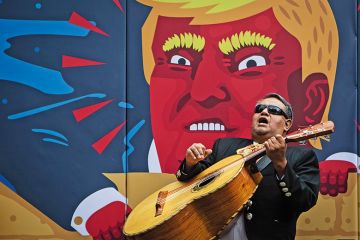 Man plays guitar in front of Donald Trump image