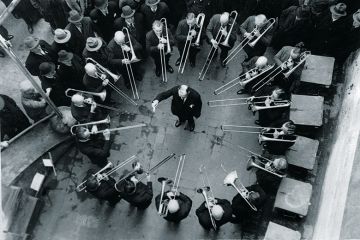 Musicians playing trombones around conductor Musicians playing trombones around conductor