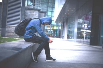 A young man in a hoodie sitting on a city street, illustrating NEETs A young man in a hoodie sitting on a city street, illustrating NEETs