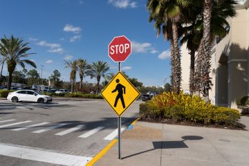 Orlando, Florida, USA - January 20, 2022 A stop sign with a Pedestrian Crossing Sign outside a shopping mall is shown in Orlando, Florida, USA.