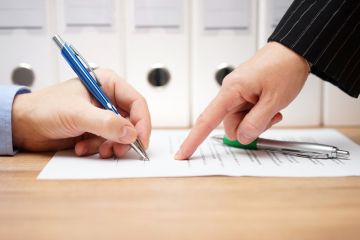 A person in a suit points to where to sign on a document
