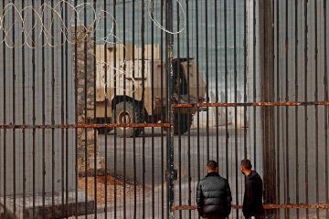 Displaced Palestinian men watch as an Egyptian army armoured personnel carrier drives near border fence between Gaza and Egypt in Rafah, in the southern Gaza Strip, amid the ongoing conflict between Israel and Hamas.
