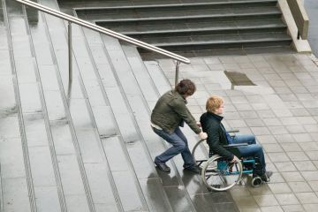 Person helping man in wheelchair up stairs Person helping man in wheelchair up stairs