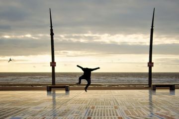 Person jumping for joy on seafront promenade