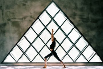 woman doing yoga by large triangular window