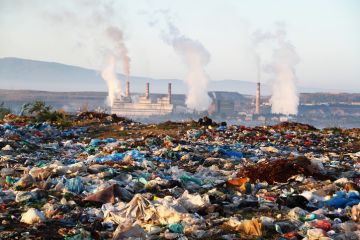 Factory chimneys behind a rubbish dump, illustrating exploitative capitalism Factory chimneys behind a rubbish dump, illustrating exploitative capitalism