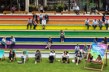 People sit on steps painted in the rainbow flag colours in support of Pride, Paddington, London. To illustrate that the public still supports EDI work in UK universities.