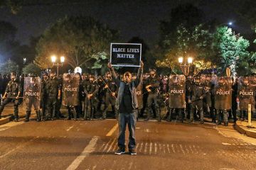 A man holds a placard saying ‘Black Lives Matter’ before a line of policemen A man holds a placard saying ‘Black Lives Matter’ before a line of policemen