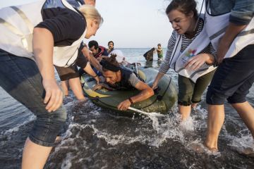 Kos, Greece - October 2015: Volunteers give a hand to migrants from Afghanistan who arrived at Kos from Turkey on a dinghy Kos, Greece - October 2015: Volunteers give a hand to migrants from Afghanistan who arrived at Kos from Turkey on a dinghy