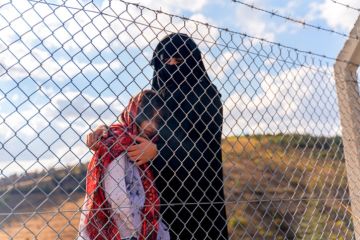 A refugee mother and her child behind a migrant camp fence