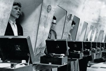 Row of men listening to vinyl records in turntable booths Row of men listening to vinyl records in turntable booths