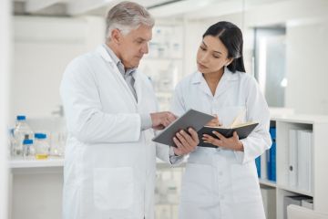 A senior scientist shows a junior scientist something on a tablet