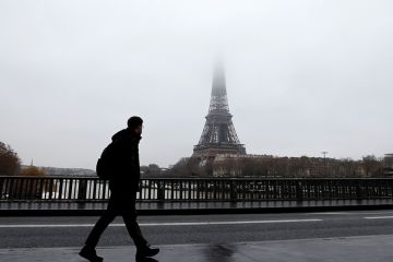A man walks on a bridge across the Seine with the Eiffel Tower in the background A man walks on a bridge across the Seine with the Eiffel Tower in the background