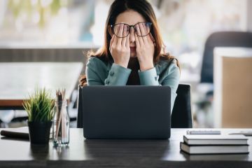 Woman looking stressed at work Woman looking stressed at a laptop with her hands over her eyes
